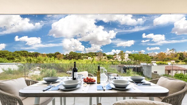 Une table à manger pour deux, avec des chaises en osier, une paroi en verre transparent et une vue pittoresque sur un village.