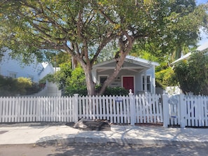 A house with a red door, white picket fence, and a tree in front.