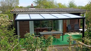 Une maison moderne dotée d’une véranda en verre, d’un revêtement extérieur en bois et d’une pelouse verdoyante.