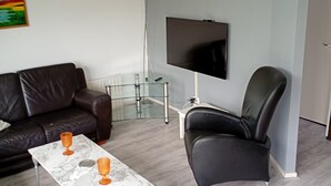 Un salon avec un canapé, une table basse, un téléviseur et un fauteuil.