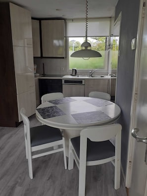 A compact kitchen with a dining area, a window with a view of greenery, and a hanging light fixture.