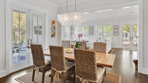 A dining area with wicker chairs, a wooden table, and a chandelier. - WaterColor on Dragonfly Park | Porches & Park Views (Santa Rosa Beach)