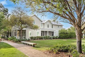 A two-story house with a covered porch, a well-maintained lawn, and a pathway leading to a bench.