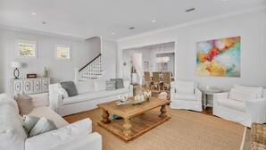 A spacious living room with a wooden coffee table, white sofas, and a staircase leading to another level. - WaterColor on Dragonfly Park | Porches & Park Views (Santa Rosa Beach)