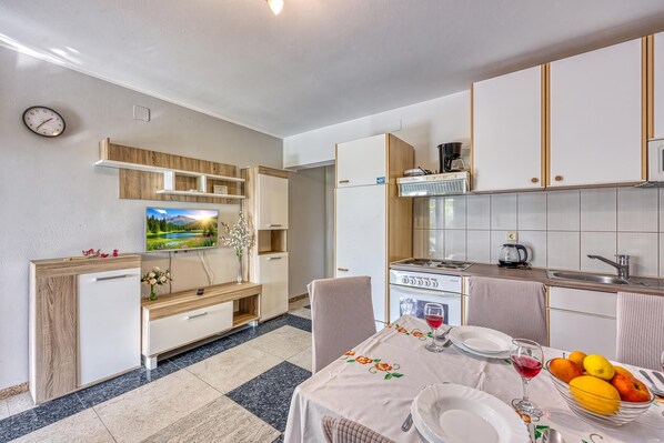A compact kitchen with a dining area, equipped with a stove, sink, and a television. - Silver Cherry Apartments (Jasenice)