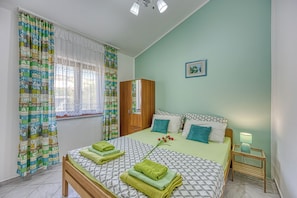 A bedroom with a bed, a wardrobe, a bedside table with a lamp, and a window with curtains.