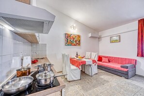 Una cocina compacta con electrodomésticos modernos, una zona de comedor con mantel rojo y un sofá gris.