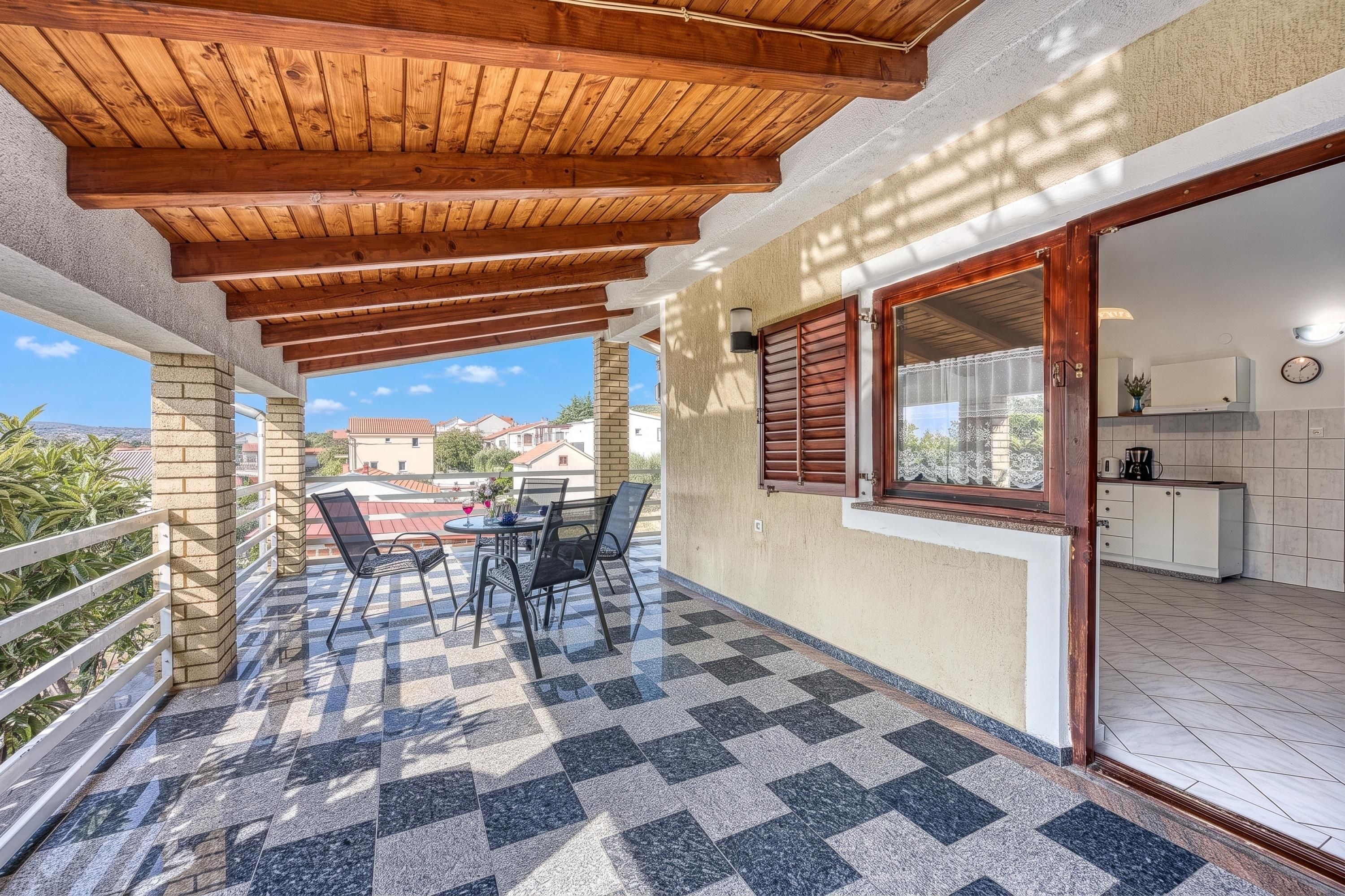 Un porxo exterior cobert amb un paviment de pissos, una taula amb cadires i vista al barri.