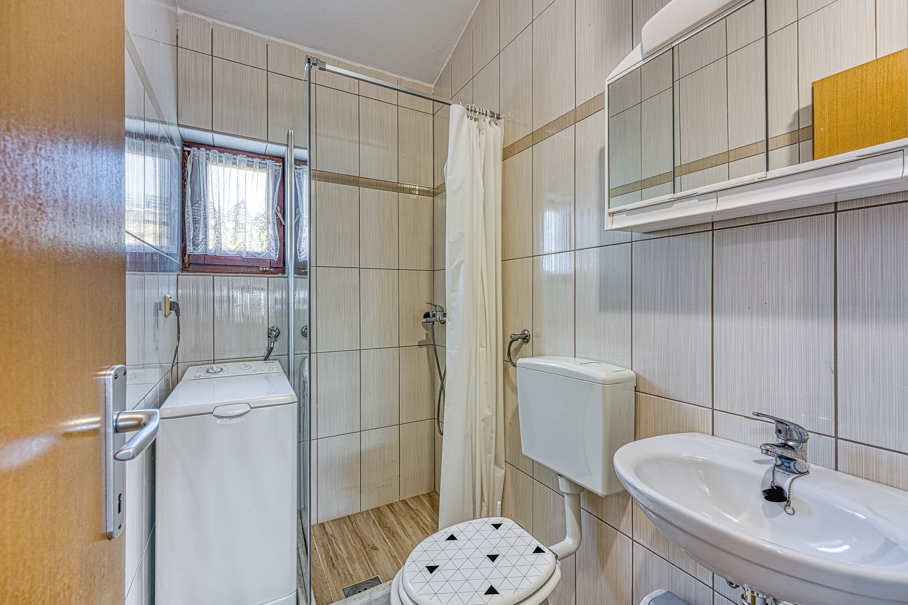 Un baño con ducha, inodoro, lavabo y una ventana con cortina.