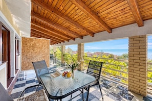 A balcony with a wooden ceiling, a glass table with chairs, a vase with flowers, and a view of the sea. - Silver Cherry Apartments (Jasenice)