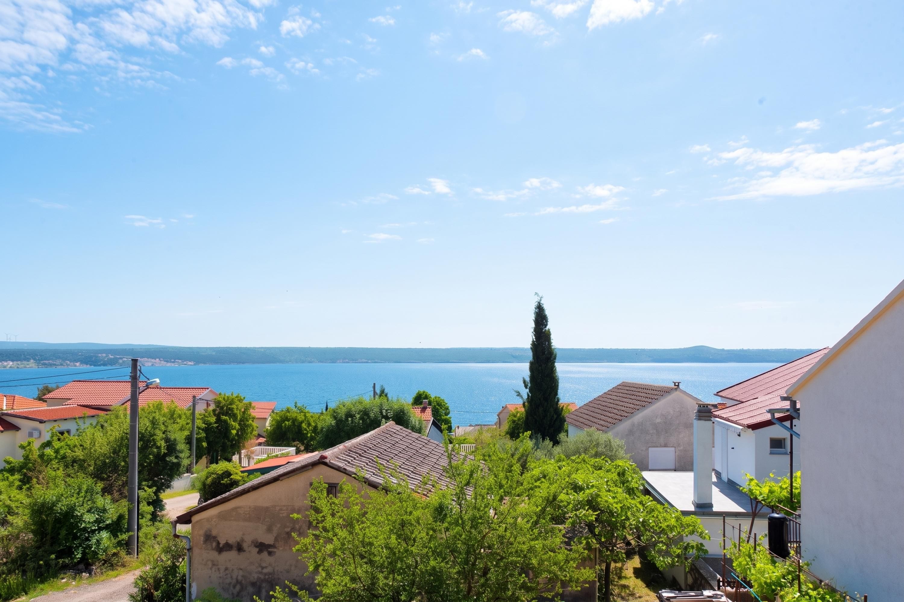 A coastal residential area with houses, a clear sky, and a view of the sea.