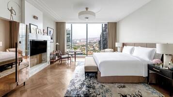 A hotel room with a large bed, a TV, a desk, and a view of the city.