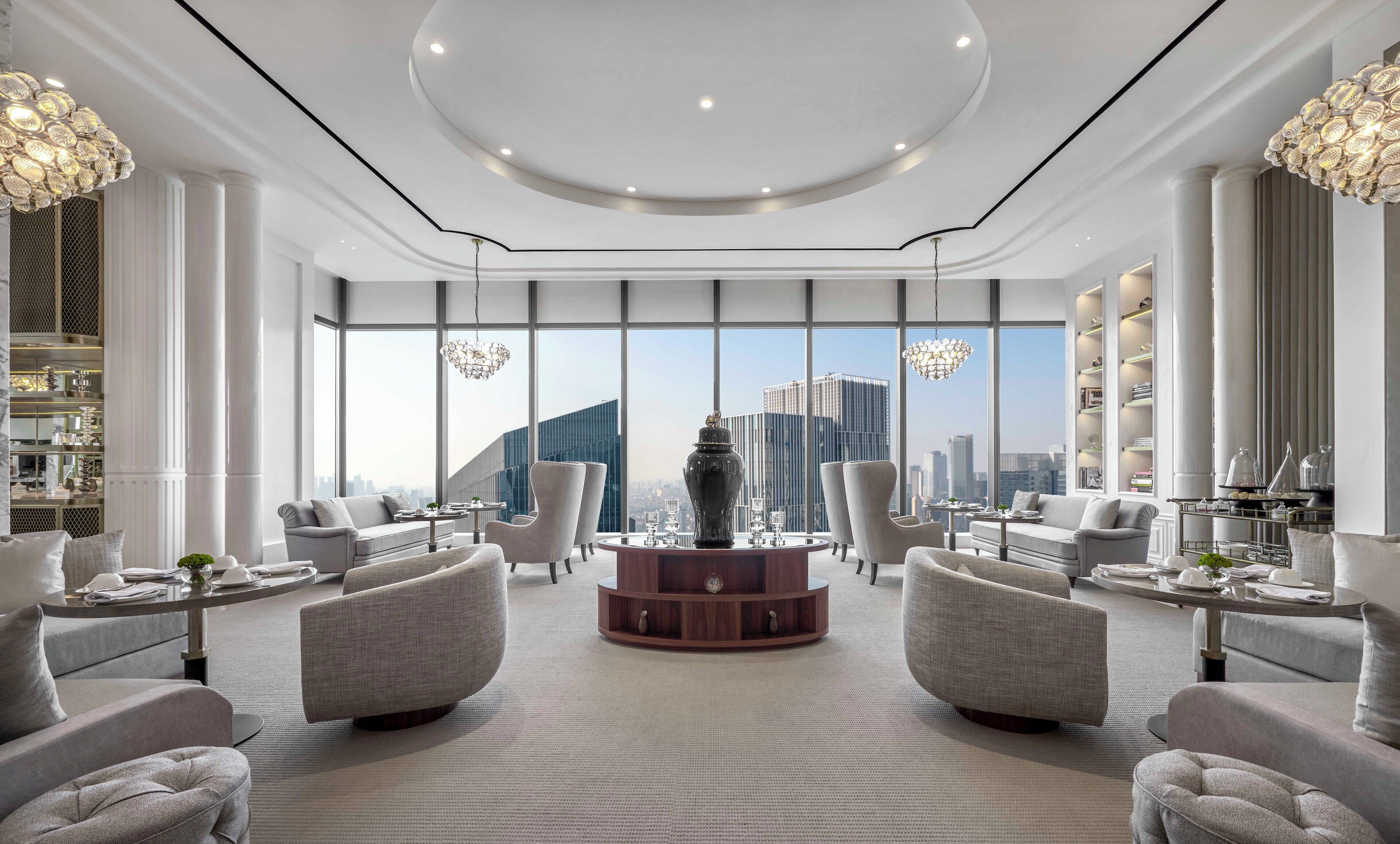 Un moderno vestíbulo de hotel con una mesa redonda central, asientos y ventanas amplias con vistas a la ciudad.