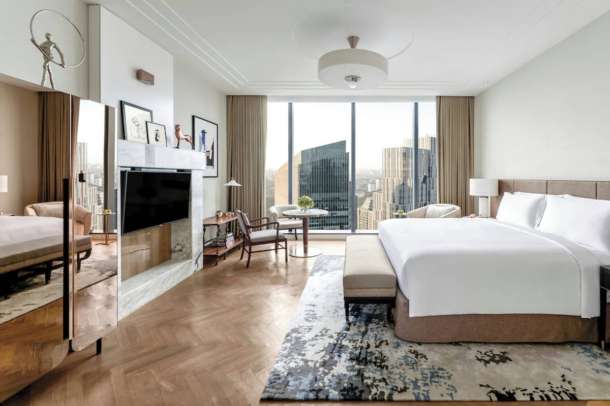 Quarto de hotel com cama, escrivaninha, televisão, cadeira, mesinha de centro e vista para a cidade.