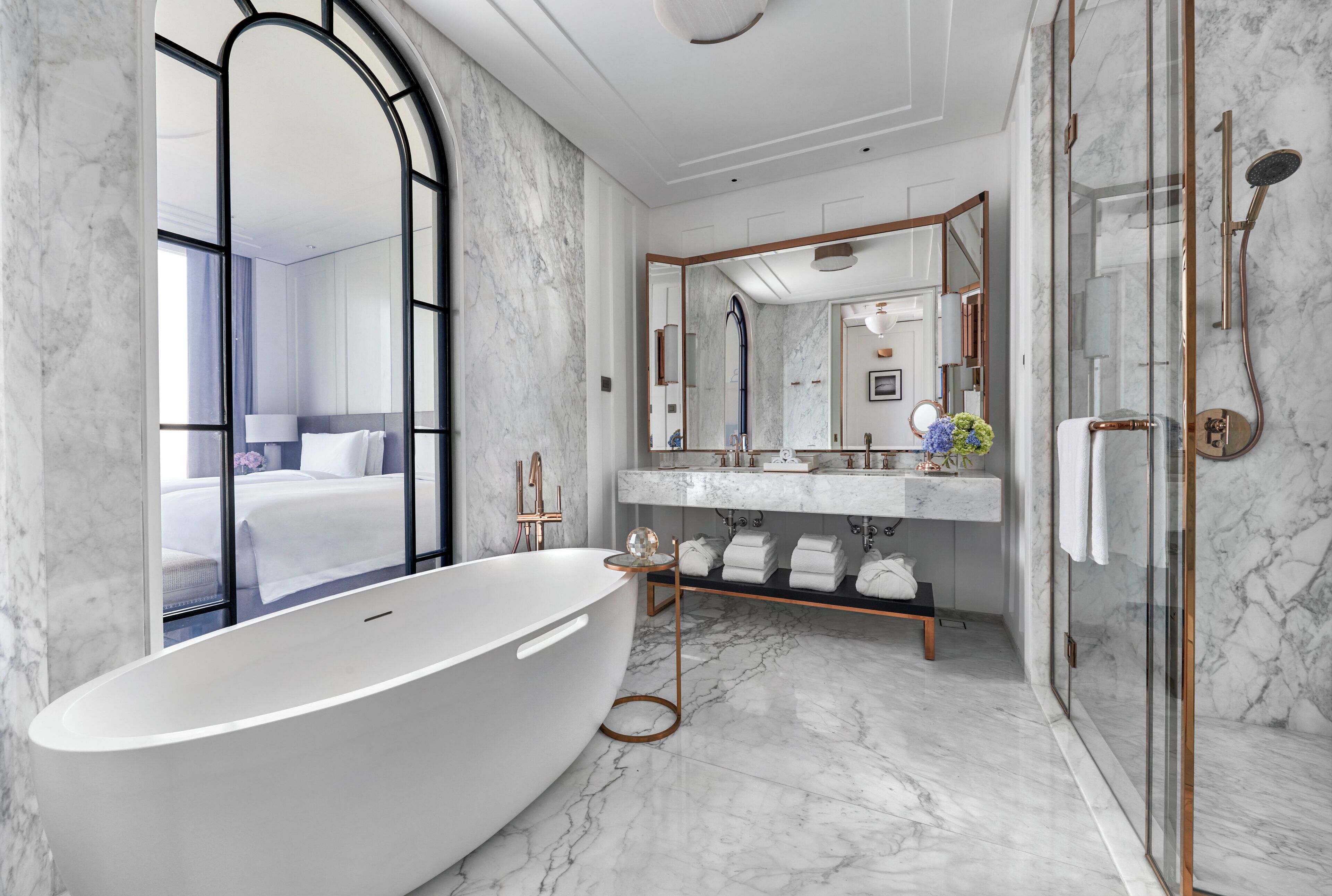 Een moderne badkamer met een vrijstaand bad, een douche met glazen wanden en een marmeren vloer.