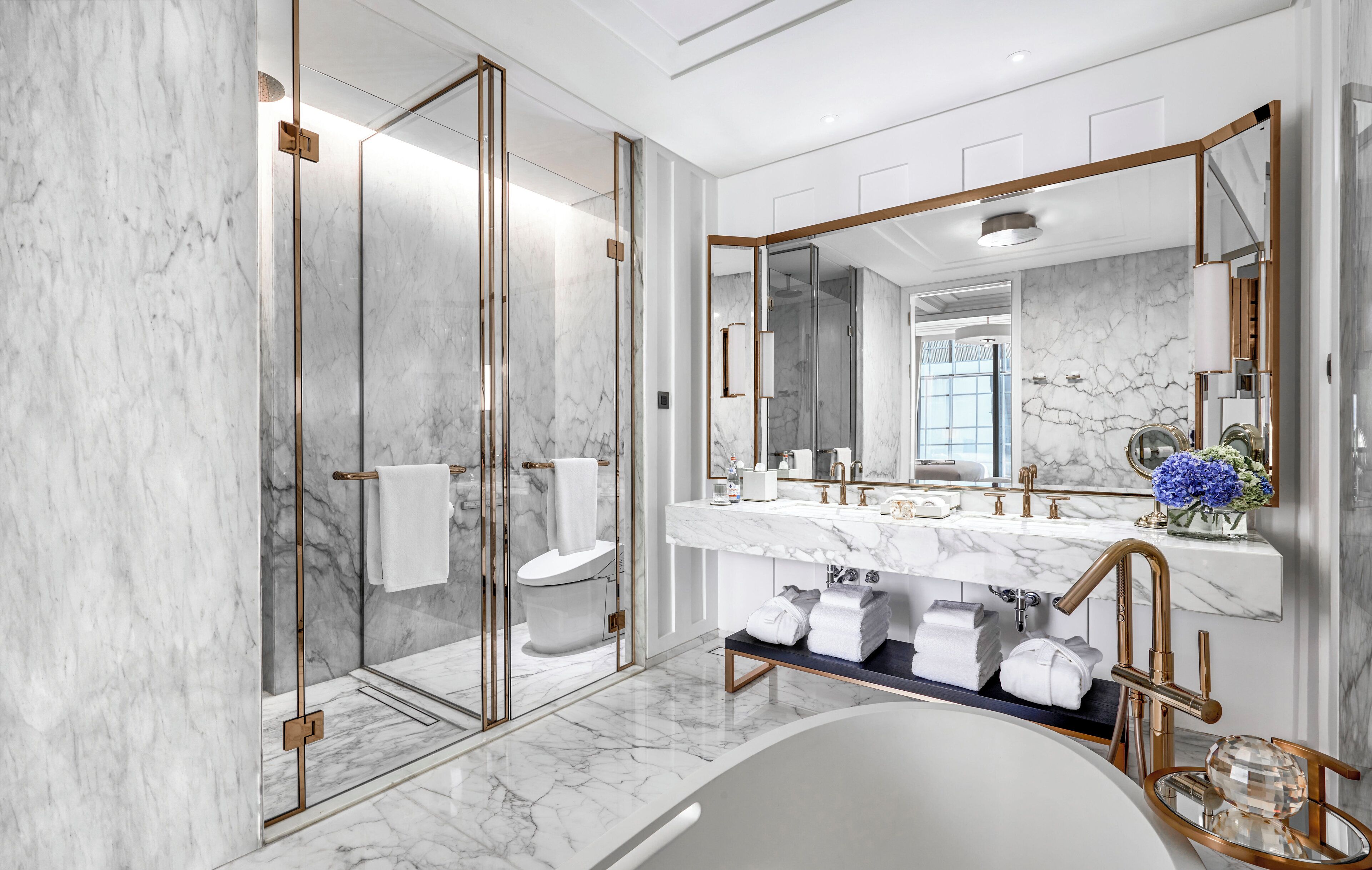 Un baño moderno con ducha envuelta en vidrio, un espejo grande y una bañera con encimera de mármol.