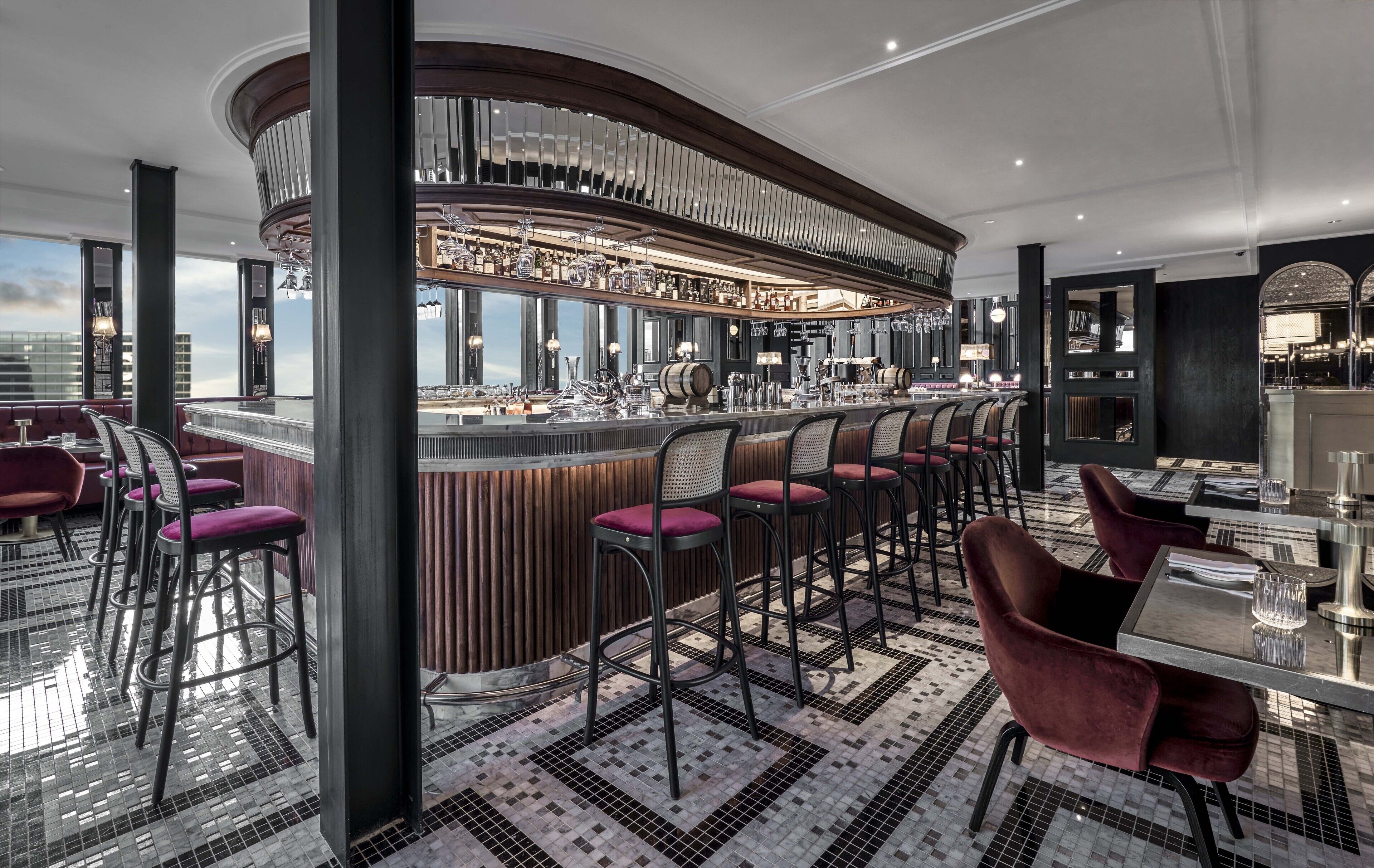 A modern bar area with a curved counter, bar stools, and a view of the cityscape.