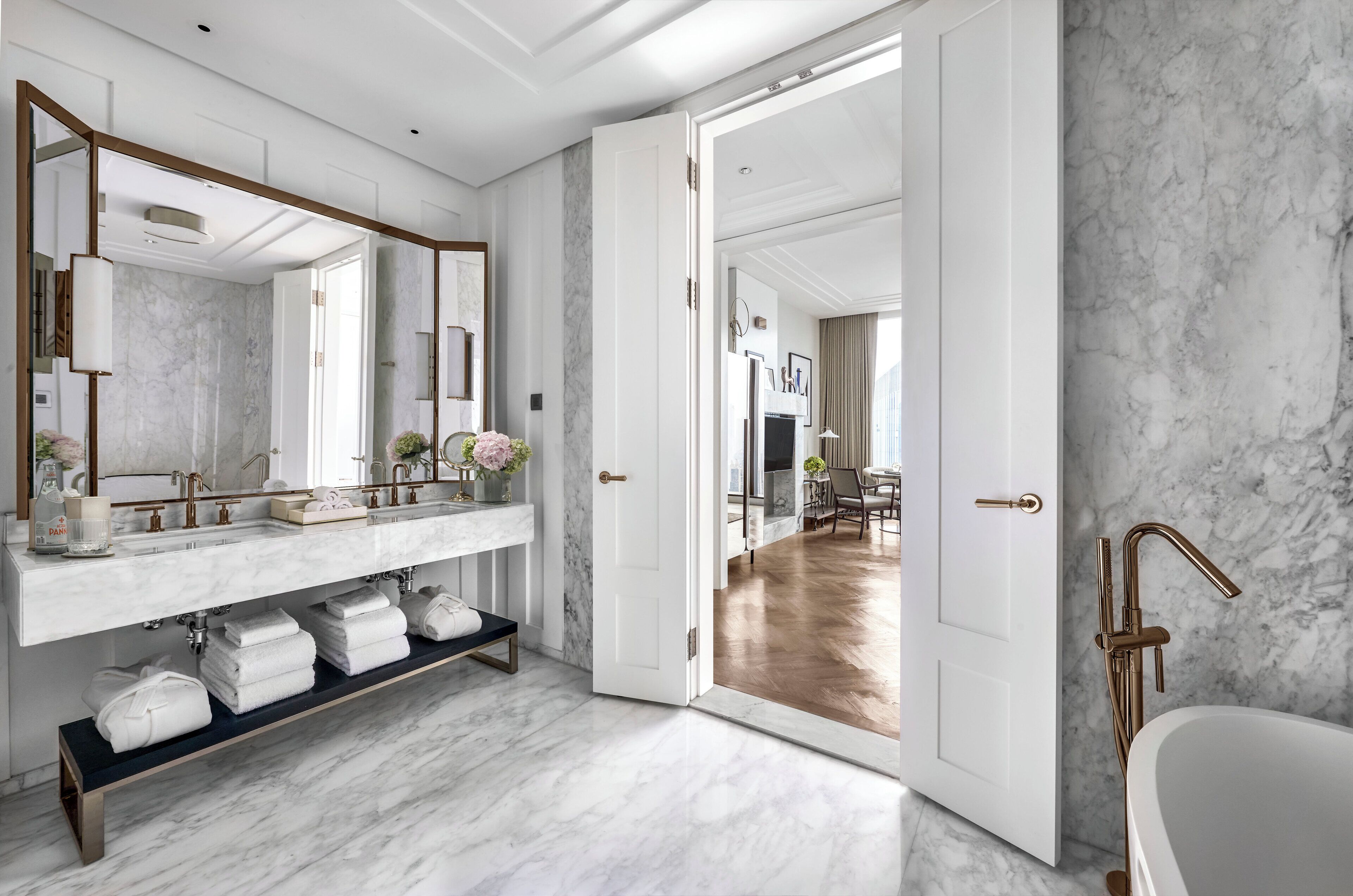 A modern bathroom with a marble vanity, a large mirror, and a bathtub.