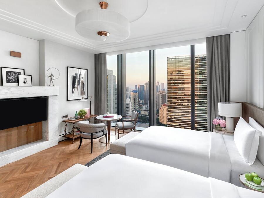 A modern hotel room with a large bed, a desk with a chair, a small table, and a fireplace.
