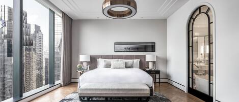 A modern hotel room with a large bed, a view of the city, a large mirror, and a circular ceiling light.