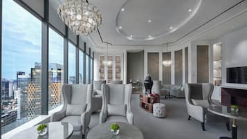 A modern living room with a city view, a round coffee table, grey upholstered chairs, a chandelier, and a fireplace.