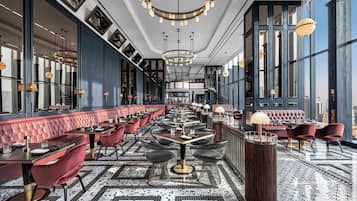 A spacious restaurant with high ceilings, large windows, and a central seating area with tables and chairs.
