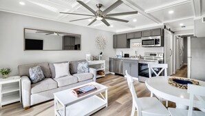 Een moderne woonkamer met een grijze bank, een witte salontafel en een plafondventilator.