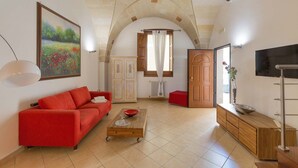 Ein Wohnzimmer mit einem roten Sofa, einem Holztisch, einem Fernseher und einem Bild von einem Feld.