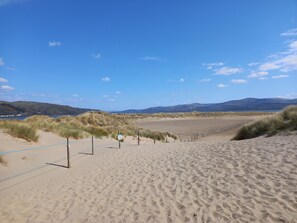 A sandy beach with a clear sky, grassy dunes, and distant mountains. - Beautifully renovated two bedroom cottage in the heart of the Dyfi Valley (Machynlleth)
