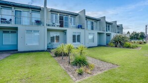 A modern multi-story building with balconies, a well-maintained lawn, and a small garden area.