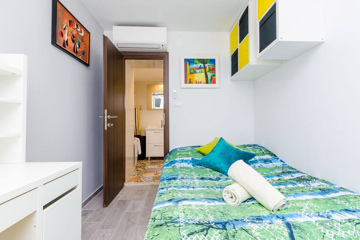 A bedroom with a bed, a white dresser, and a door leading to a bathroom.