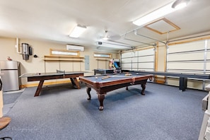 Une table de billard avec des queues et des billes, une table de ping-pong et un réfrigérateur.