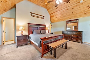 Une chambre à coucher avec un plafond en bois, un lit avec une tête de lit, des tables de chevet avec des lampes, une commode et un banc.