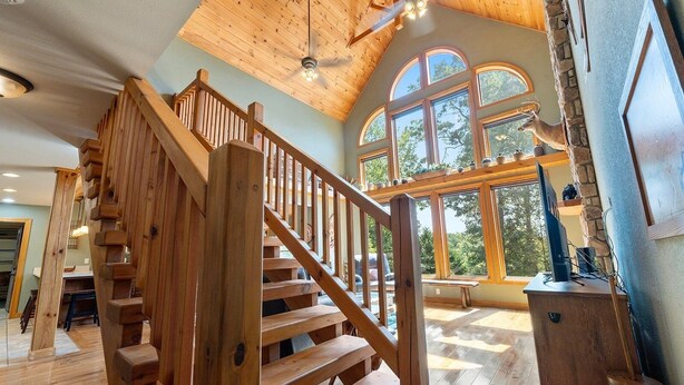 Un escalier en bois mène à une mezzanine dotée de grandes fenêtres et d’un ventilateur de plafond.