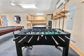 A foosball table in a room with a pool table, wooden cabinets, and a fire extinguisher on the wall.