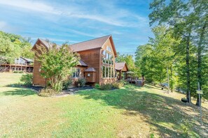 Une maison en bois à deux étages, dotée d’un toit en pente, entourée d’une pelouse bien entretenue et d’arbres.