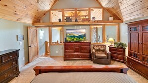 Une chambre spacieuse avec un grand lit, un plafond en bois et une télévision.