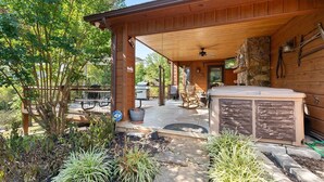 Un patio couvert doté d’une cheminée en pierre, de sièges d’extérieur et offrant une vue sur le jardin environnant.