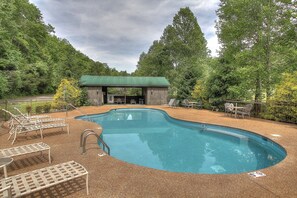 A swimming pool with lounge chairs and a covered seating area, surrounded by trees.