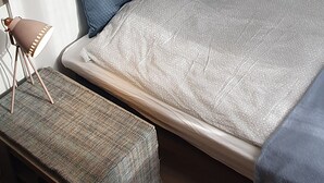 Un dormitorio con una cama, una lámpara de noche, una lámpara colgante y un banco.