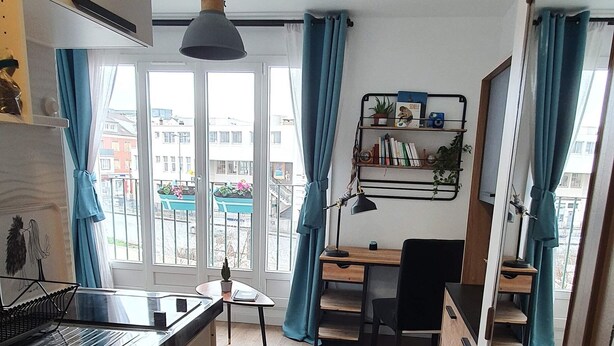 Una cocina moderna con suelo de madera, un comedor con mesa y sillas, y vista a la ciudad a través de amplias ventanas.