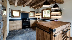 A kitchen with a stone floor, wooden cabinets, a black stove, and pendant lights. - Chalet Pain Seigle (Riddes)