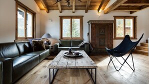 A cozy living room with a wooden ceiling, a leather sofa, a wooden coffee table, and a blue folding chair. - Chalet Pain Seigle (Riddes)