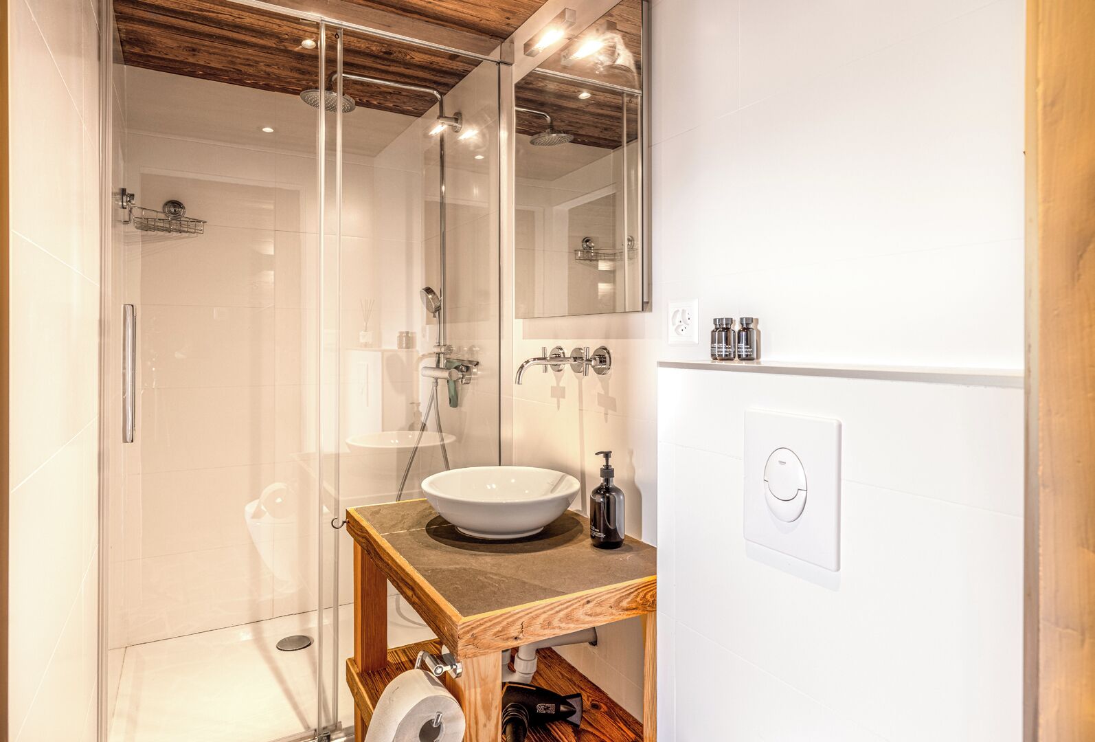 Een moderne badkamer met een douchecabine van glas, een houten wastafelmeubel met een witte wastafel en een grote spiegel.