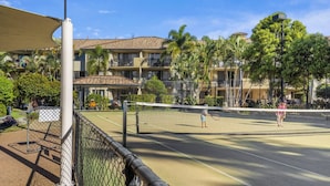 An outdoor tennis court with a net, surrounded by a chain-link fence, and adjacent to a building with balconies. - 2-Bed Family Haven with Pools, BBQ & Playgrounds (Mermaid Beach)