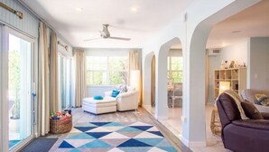 Un vaste espace de vie agrémenté d’un tapis à motifs géométriques, d’un canapé blanc, d’un canapé en cuir marron et d’un ventilateur de plafond.