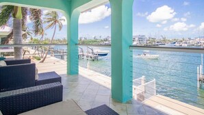 Un espace extérieur abrité, doté de mobilier en osier, offrant une vue sur le port de plaisance et un ciel dégagé.