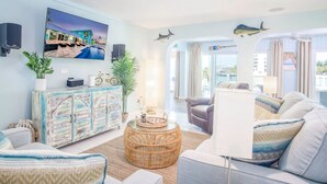 Un salon moderne doté d’un grand téléviseur, de sièges confortables, d’un meuble décoratif et offrant une vue sur l’extérieur.