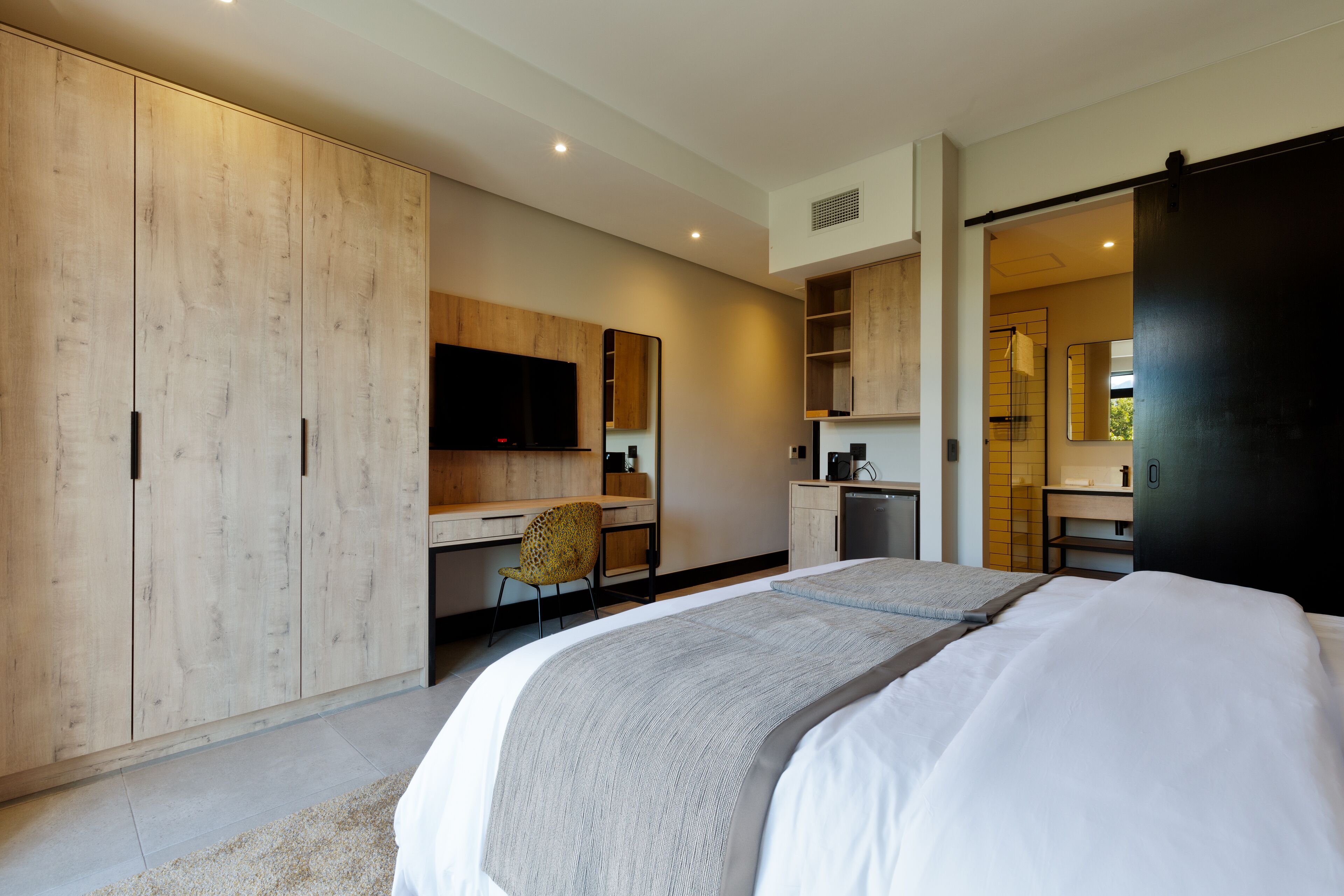 Una habitación de hotel moderna con una cama grande, un escritorio, una silla y un armario.