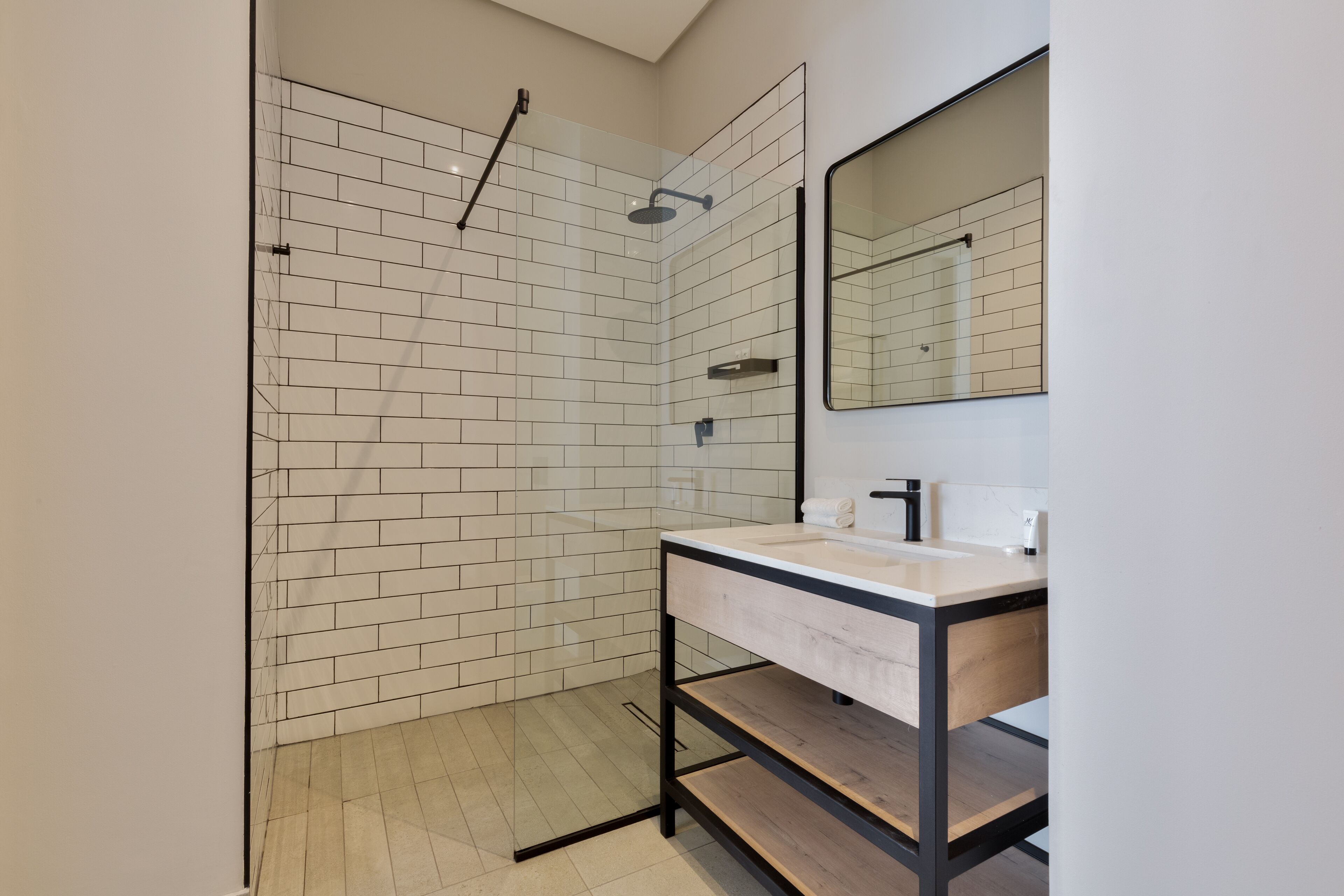 A modern bathroom with a glass shower enclosure, a wooden vanity with a sink, and a large mirror.